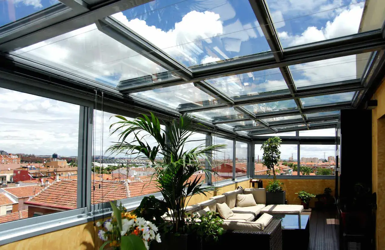 Un cerramiento ático con sofás y plantas, disfrutando de vistas urbanas bajo un cielo nublado.