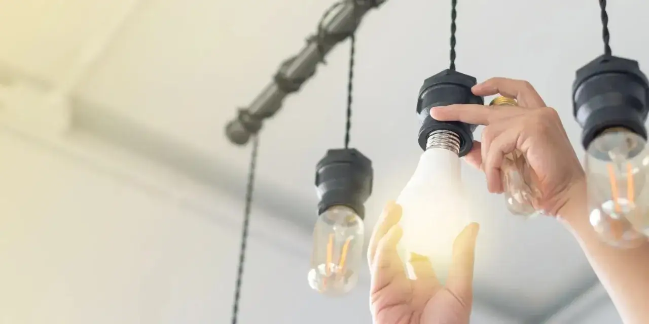 Manos cambian una bombilla LED en una l&aacute;mpara colgante, reemplazando una antigua. La nueva luz ilumina el espacio.