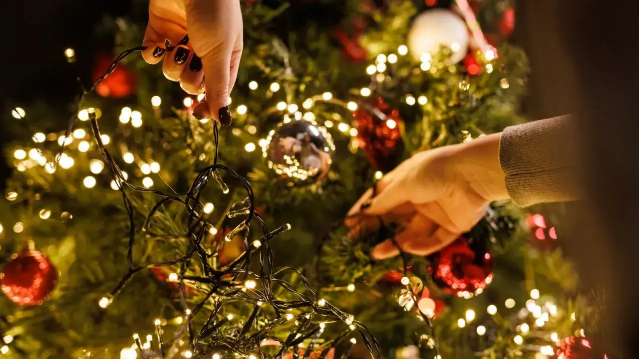 Manos decoran un árbol de Navidad con luces cálidas. ¿Cuánto consumen las luces de Navidad?