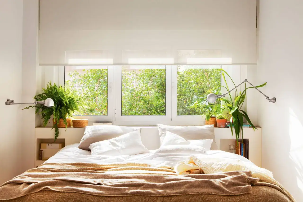 Un dormitorio acogedor con plantas para el dormitorio, cama con mantas y almohadas, y una ventana con vistas a la vegetación.