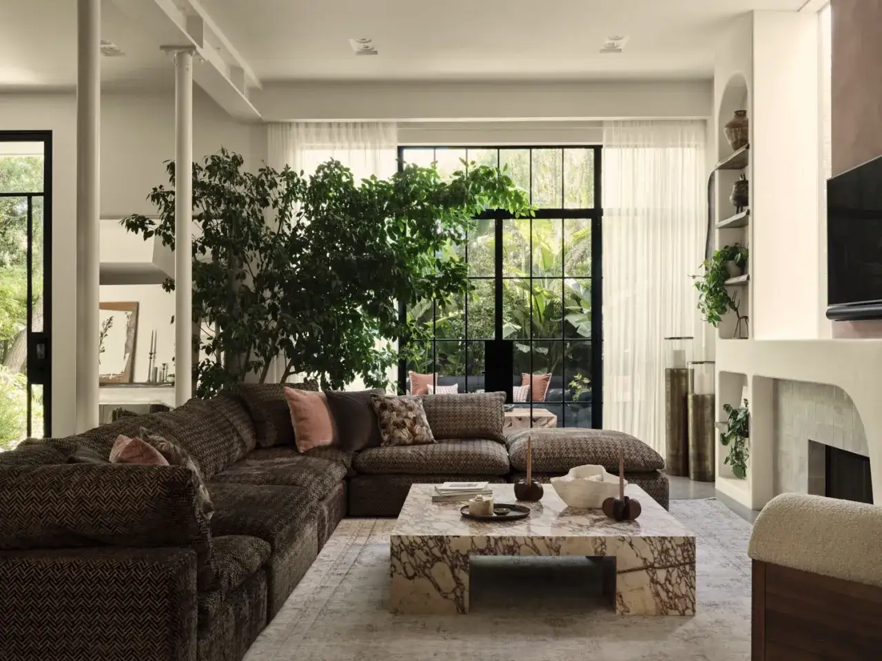 Un acogedor rincón de plantas en el salón, con un gran sofá marrón, mesa de centro de mármol y ventanales que conectan con la naturaleza.