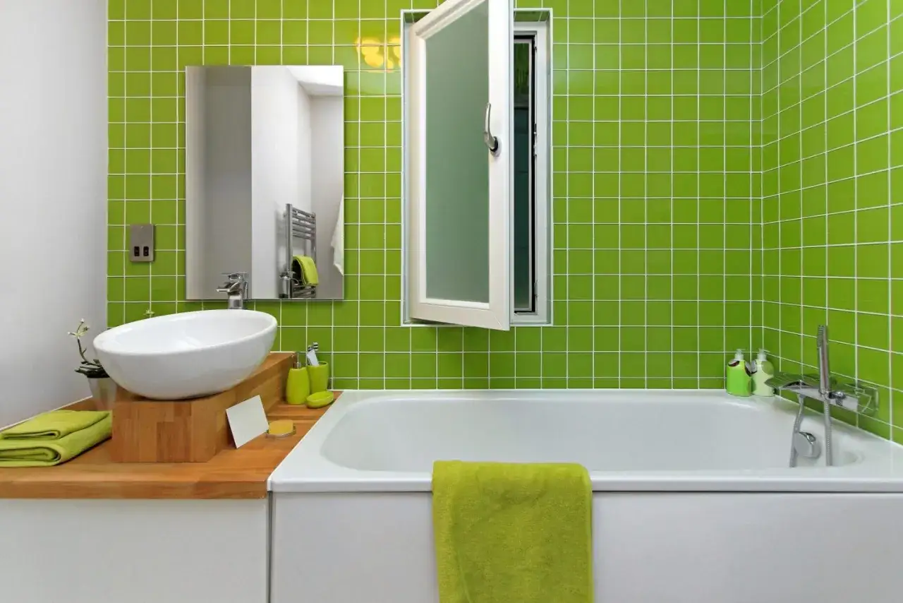 Ideas para pintar azulejos baño: un baño moderno con azulejos verdes brillantes, bañera blanca, lavabo ovalado y toallas a juego.