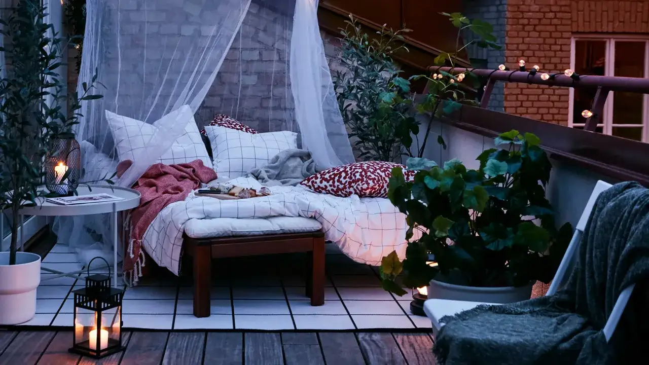 Acogedor balcón pequeño con cama, cojines, mantas, plantas y luces cálidas, ideal para relajarse.