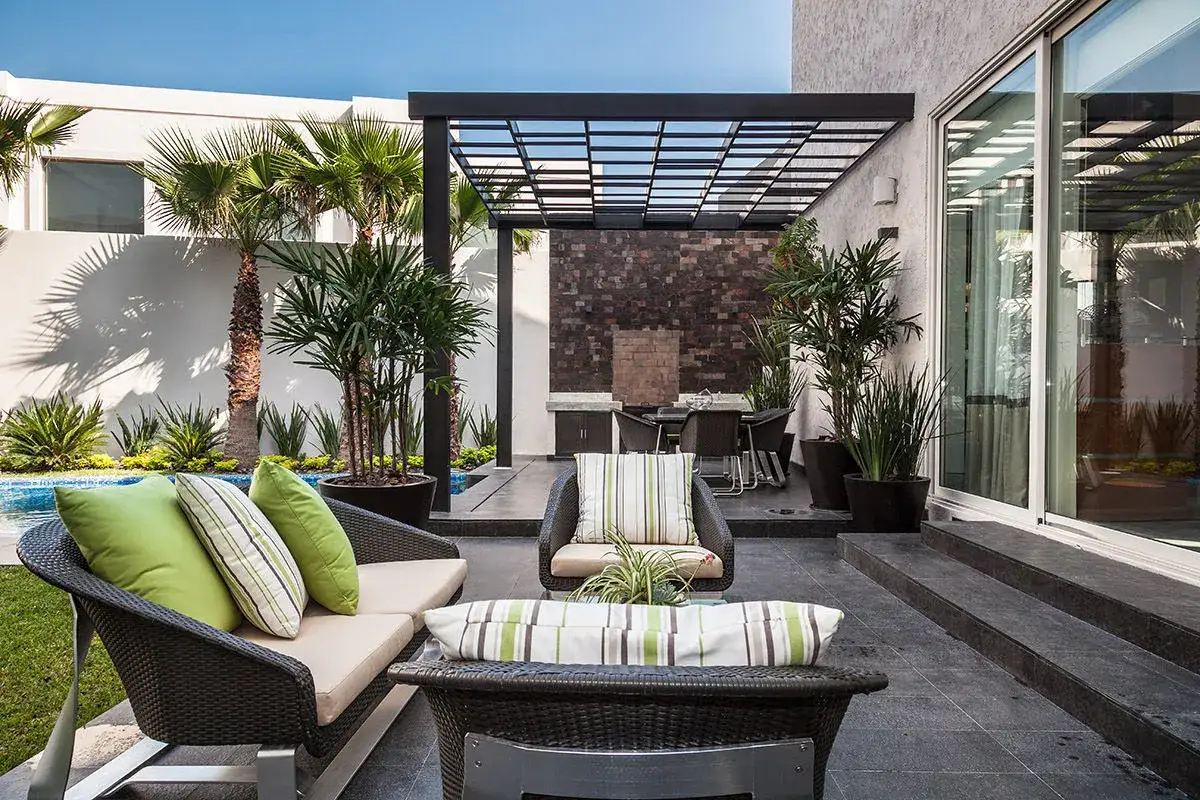 Un espacio de relajación en un jardín moderno con muebles cómodos, palmeras y una piscina azul.