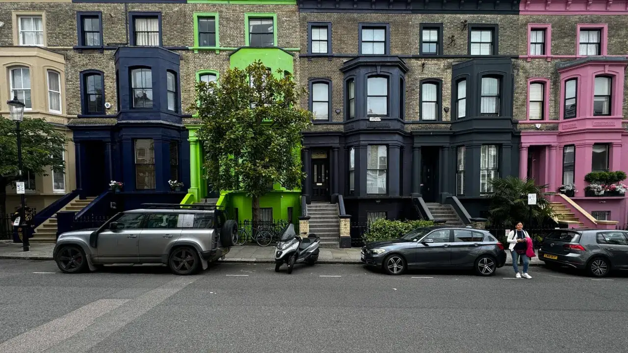 Fila de casas de colores en Londres, con fachadas azul marino, verde brillante y rosa vibrante. Coches aparcados en la calle.