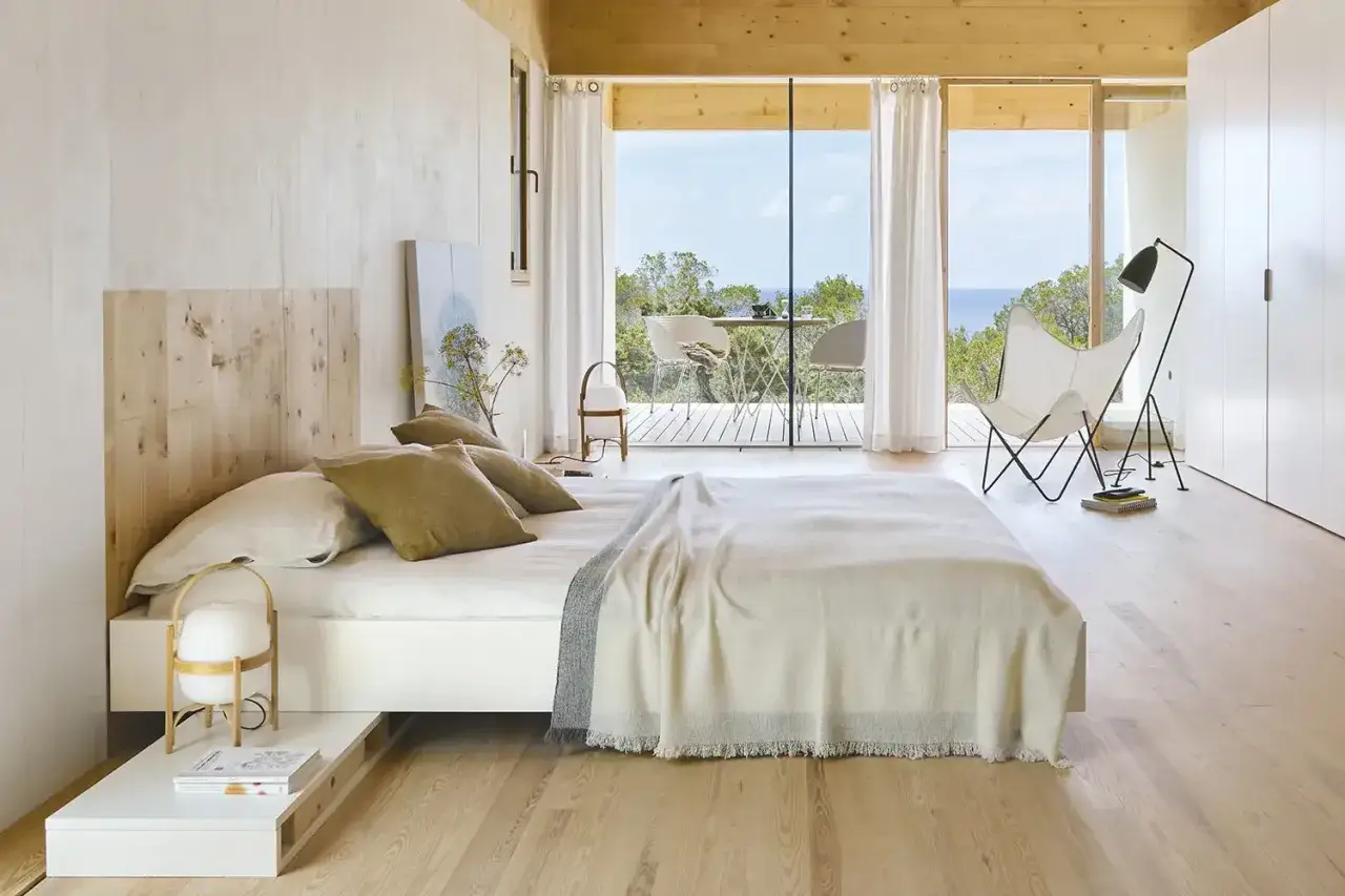 Habitaci&oacute;n moderna con cama, sill&oacute;n mariposa y vistas al mar. Ideal para dormir en habitaci&oacute;n reci&eacute;n pintada, con luz natural y aire fresco.
