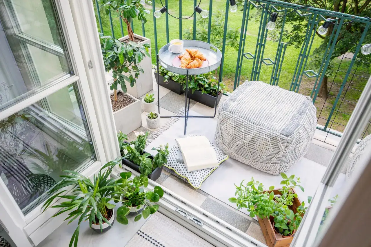Acogedor balcón con plantas, cojines, un puf y un café con cruasanes. Un rincón perfecto para disfrutar de terrazas pequeñas con encanto.