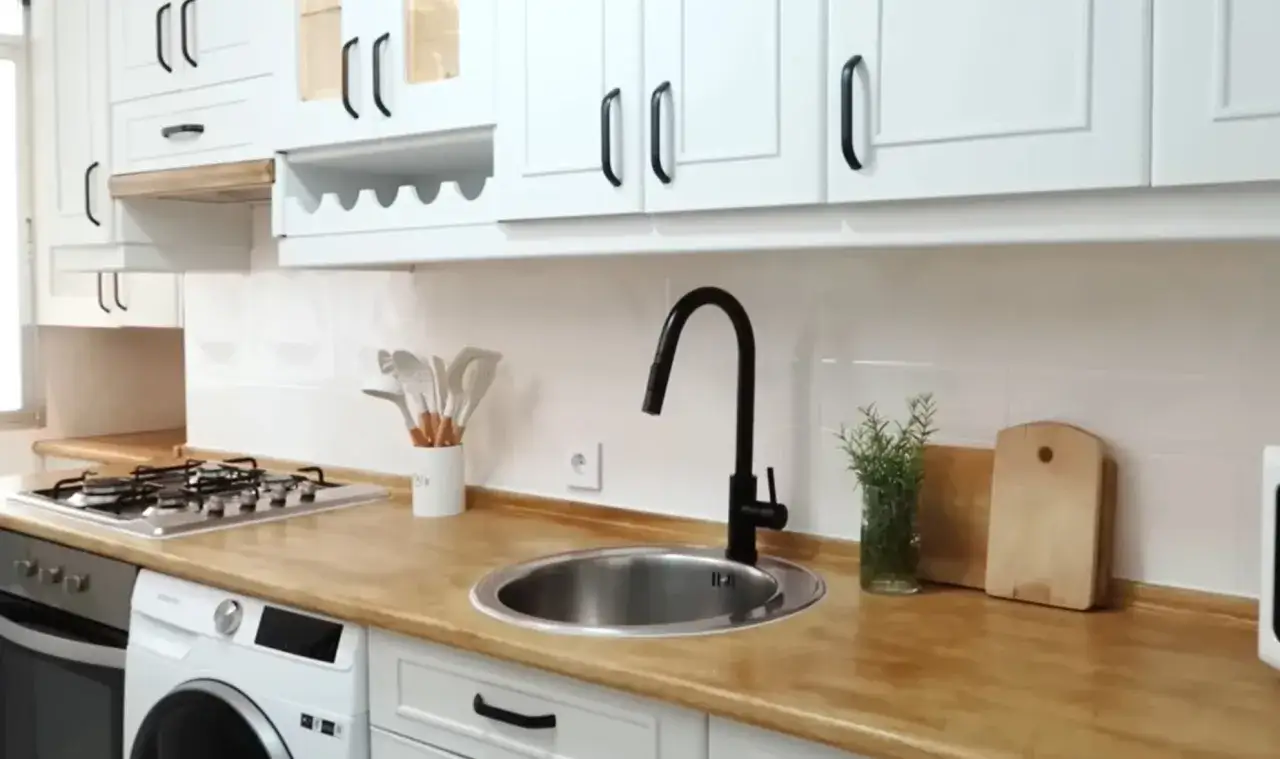 Cocina moderna con gabinetes blancos y encimeras de madera. El fregadero de acero inoxidable y el grifo negro son perfectos para pintar cocinas.