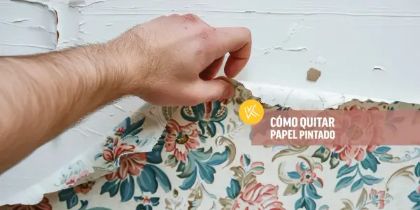 Mano retirando papel pintado floral de una pared blanca. Aprende cómo quitar papel pintado sin dañar la pared.