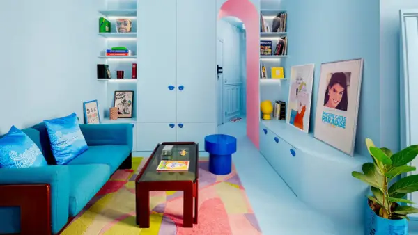 Salón pequeño con sofá azul, alfombra geométrica y estanterías llenas de objetos. Los colores pastel y vibrantes son ideales como colores para pintar salones pequeños.
