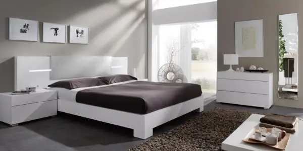 Habitación con muebles blancos y color pared neutro. Cama moderna, mesitas de noche, cómoda y espejo.
