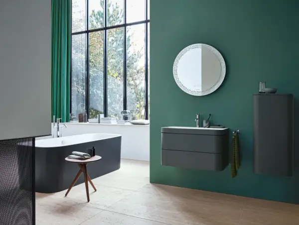Un baño moderno con bañera oscura, lavabo flotante y espejo decorativo. La pared verde es un lienzo perfecto para pintar el baño.