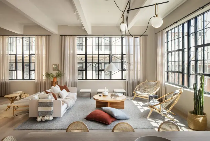 Salón con estilo industrial nórdico: sofá blanco, mesas de centro de madera, sillas de ratán y grandes ventanales.